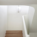 Clérachic white glass pendant hanging above an oak staircase with a curved white handrail, in a bright minimal stairwell.