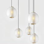 Five matte white Clérachic ribbed glass pendants of varying sizes hanging at different heights, each with a brass-toned base ring.