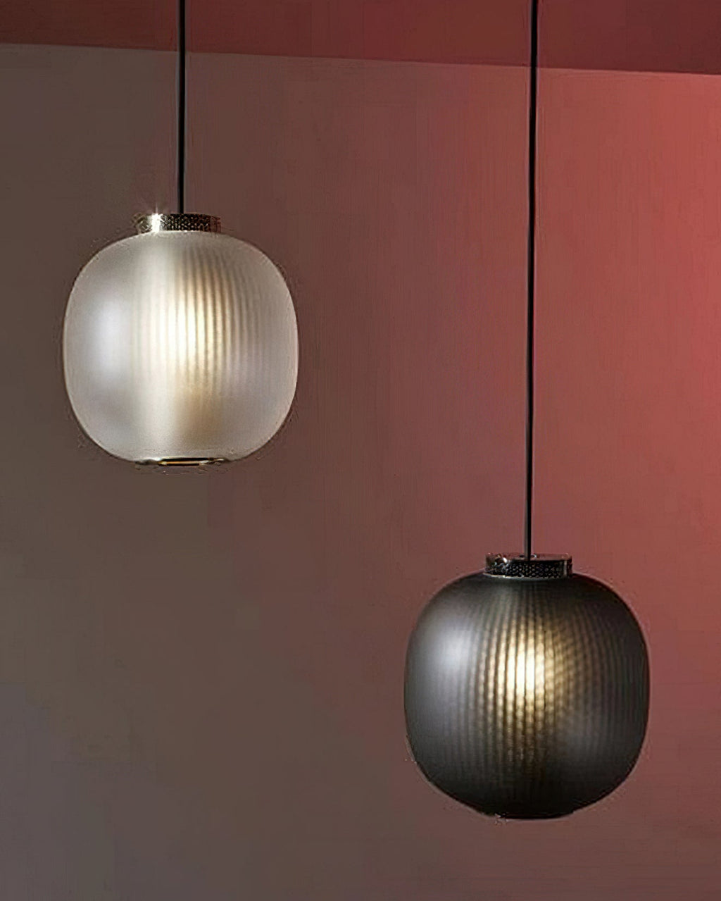 Matte white and smoke-grey Clérachic pendants lit together against a deep red wall, the ribbing visible in the glass.