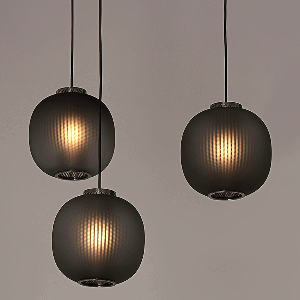 Three smoke-grey Clérachic ribbed pendants glowing warmly, hung at staggered heights against a soft taupe backdrop.