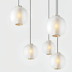 Five matte white Clérachic pendants hung close together, with brass-toned rings at the base and a warm bulb glow inside the glass.