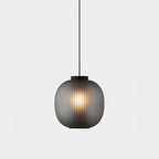 Smoke-grey Clérachic ribbed glass pendant with a black cap, lit warmly against a pale grey wall.