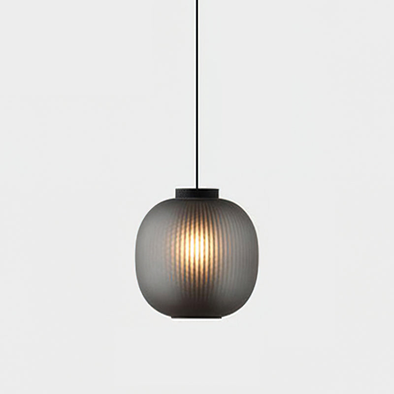Smoke-grey Clérachic ribbed glass pendant with a black cap, lit warmly against a pale grey wall.