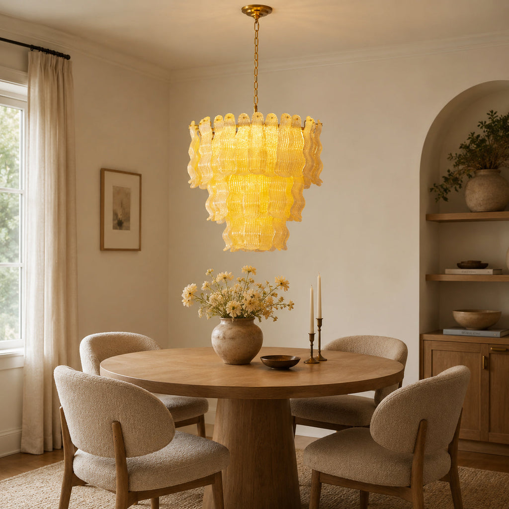 Glowing yellow Clérachic pendant above a round wooden dining table with cream chairs, beside an arched alcove with shelves.