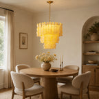 Glowing yellow Clérachic pendant above a round wooden dining table with cream chairs, beside an arched alcove with shelves.