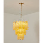 Lit yellow Clérachic pendant hung from a brass canopy and chain in the corner of a plain white room, its three tiers glowing.