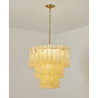 Lit Clérachic pendant in a softer yellow, three tiers of rippled glass panels on a brass chain in a white room.
