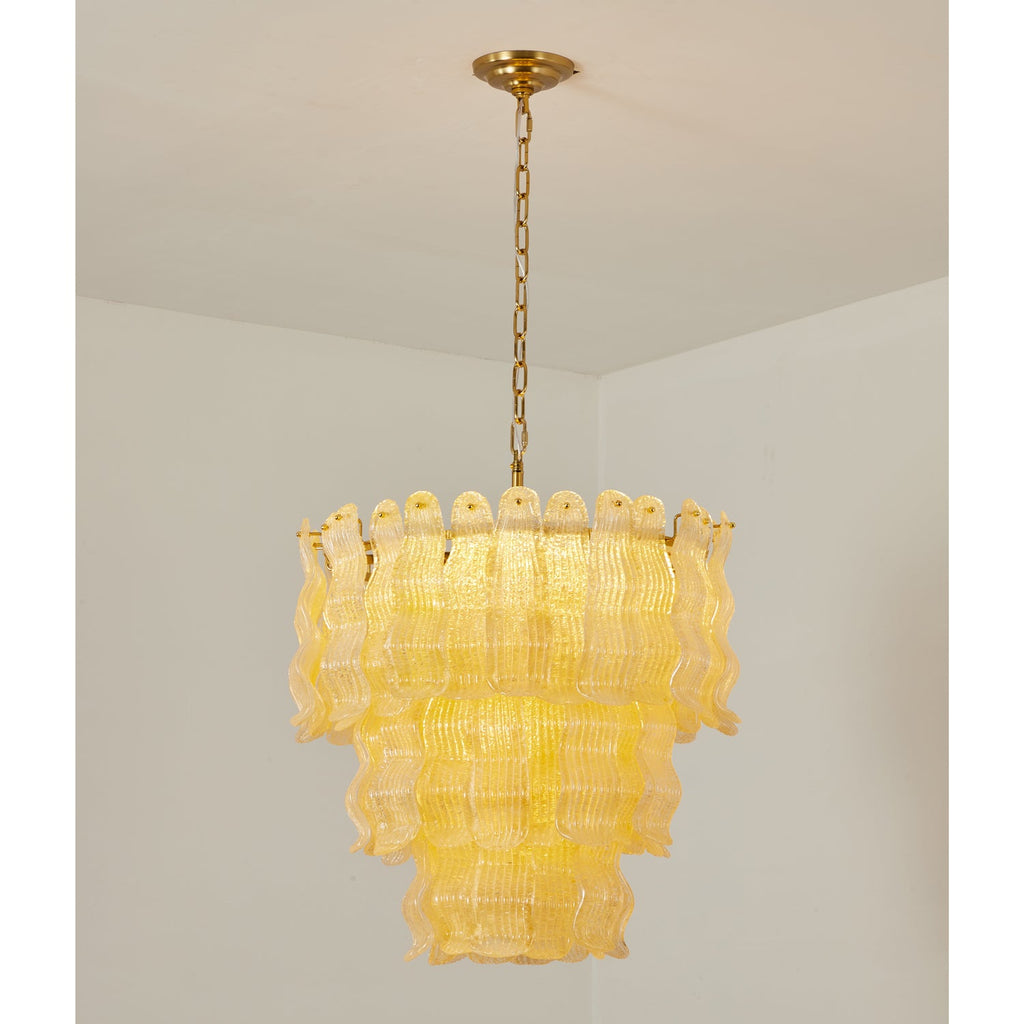 Yellow Clérachic pendant glowing in a white room corner, the wavy glass panels warm against the brass chain and canopy.