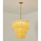 Yellow Clérachic pendant glowing in a white room corner, the wavy glass panels warm against the brass chain and canopy.