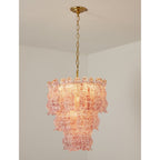 Pink Clérachic pendant lit in a white room corner, its glass flecked with red and rose, hung from a brass chain.