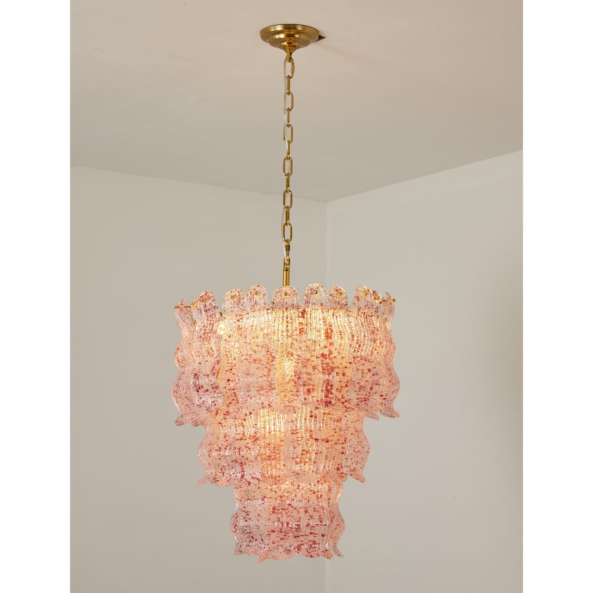 Pink Clérachic pendant lit in a white room corner, its glass flecked with red and rose, hung from a brass chain.