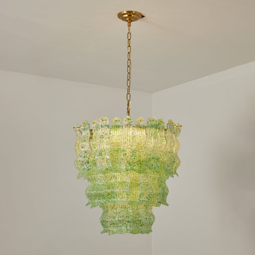 Green Clérachic pendant lit in a white room corner, the glass flecked with darker green and the tiers glowing yellow-green.