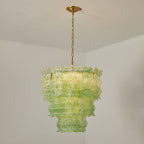 Green Clérachic pendant lit in a white room corner, the glass flecked with darker green and the tiers glowing yellow-green.