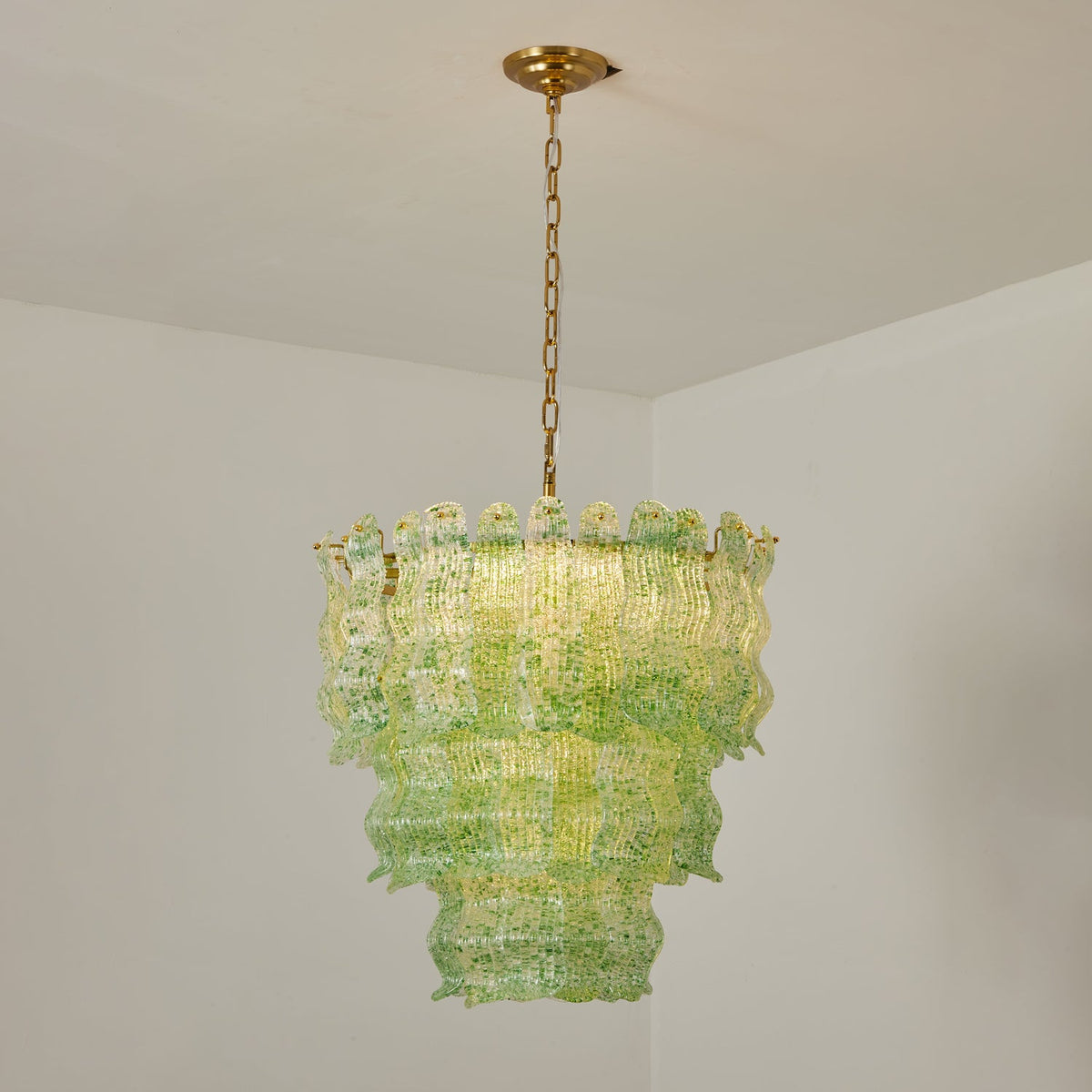 Green Clérachic pendant lit in a white room corner, the glass flecked with darker green and the tiers glowing yellow-green.