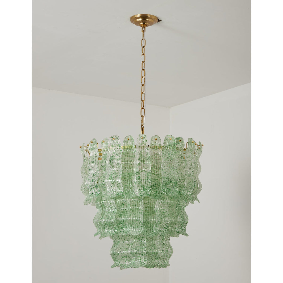 Green Clérachic pendant switched off, its pale green speckled glass tiers hung on a brass chain in a white room.