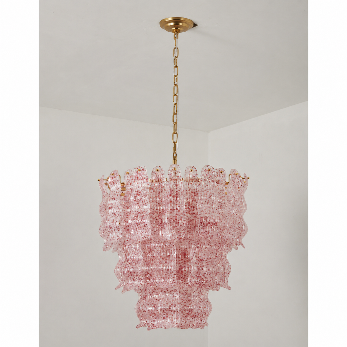 Pink speckled glass Clérachic pendant on a grey backdrop, three wavy tiers under a round brass canopy.