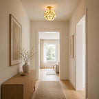 White glass-petal Clérachic ceiling light lit warm in a hallway with a wooden sideboard and a view through to a window.