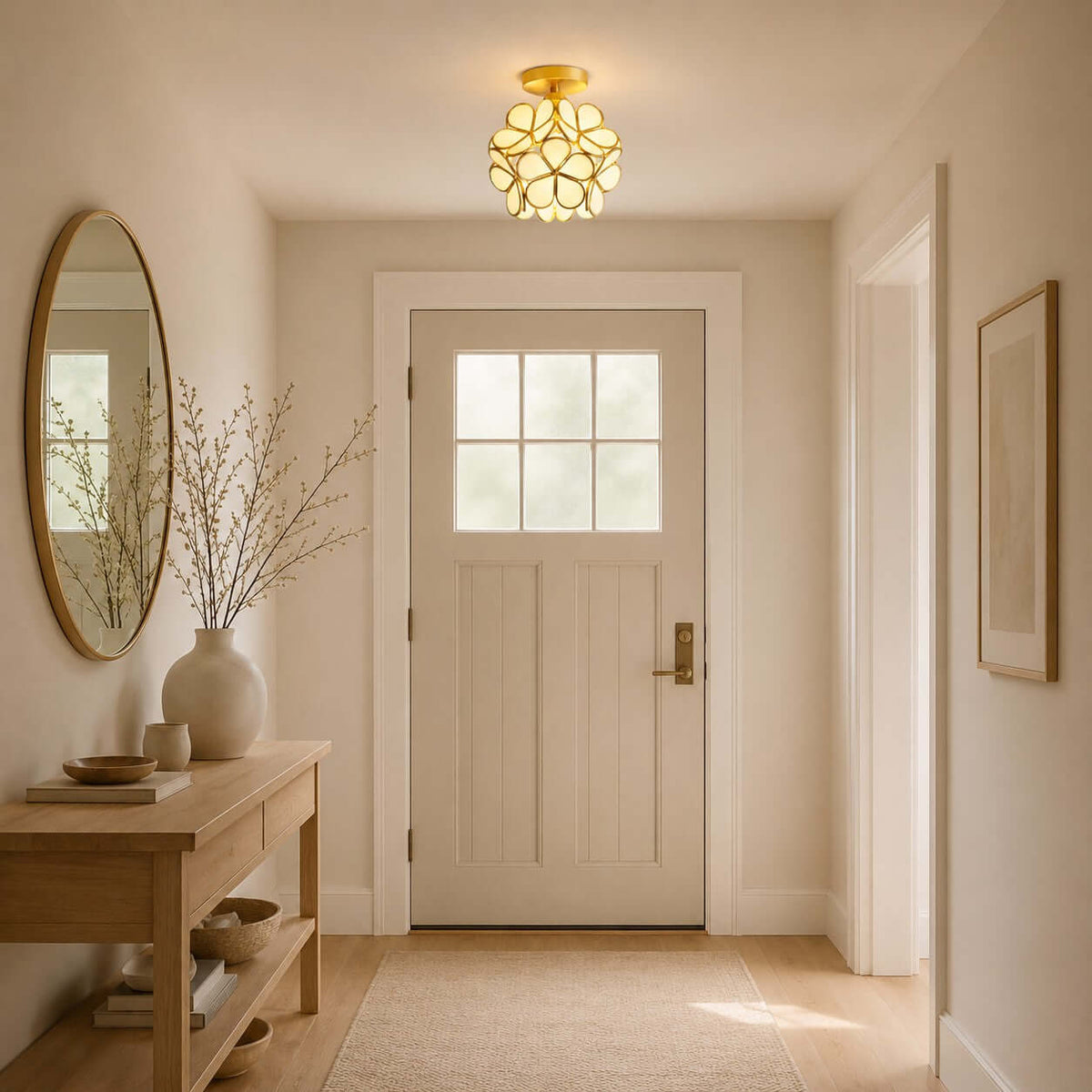 Warm white Clérachic petal light above an entrance hall with a panelled white door, a brass mirror and a bare-branch vase.