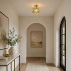 Clear glass-petal Clérachic ceiling light with a brass frame, glowing in a hall with an arched passage and a black door.