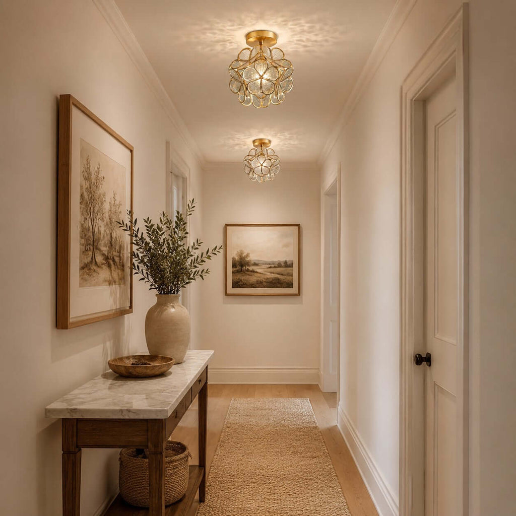 Two clear-petal Clérachic ceiling lights down a narrow hallway, with a marble-topped console and framed landscapes.