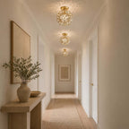 Three clear glass-petal Clérachic ceiling lights in a row along a long hallway, with a vase of olive branches on a console.