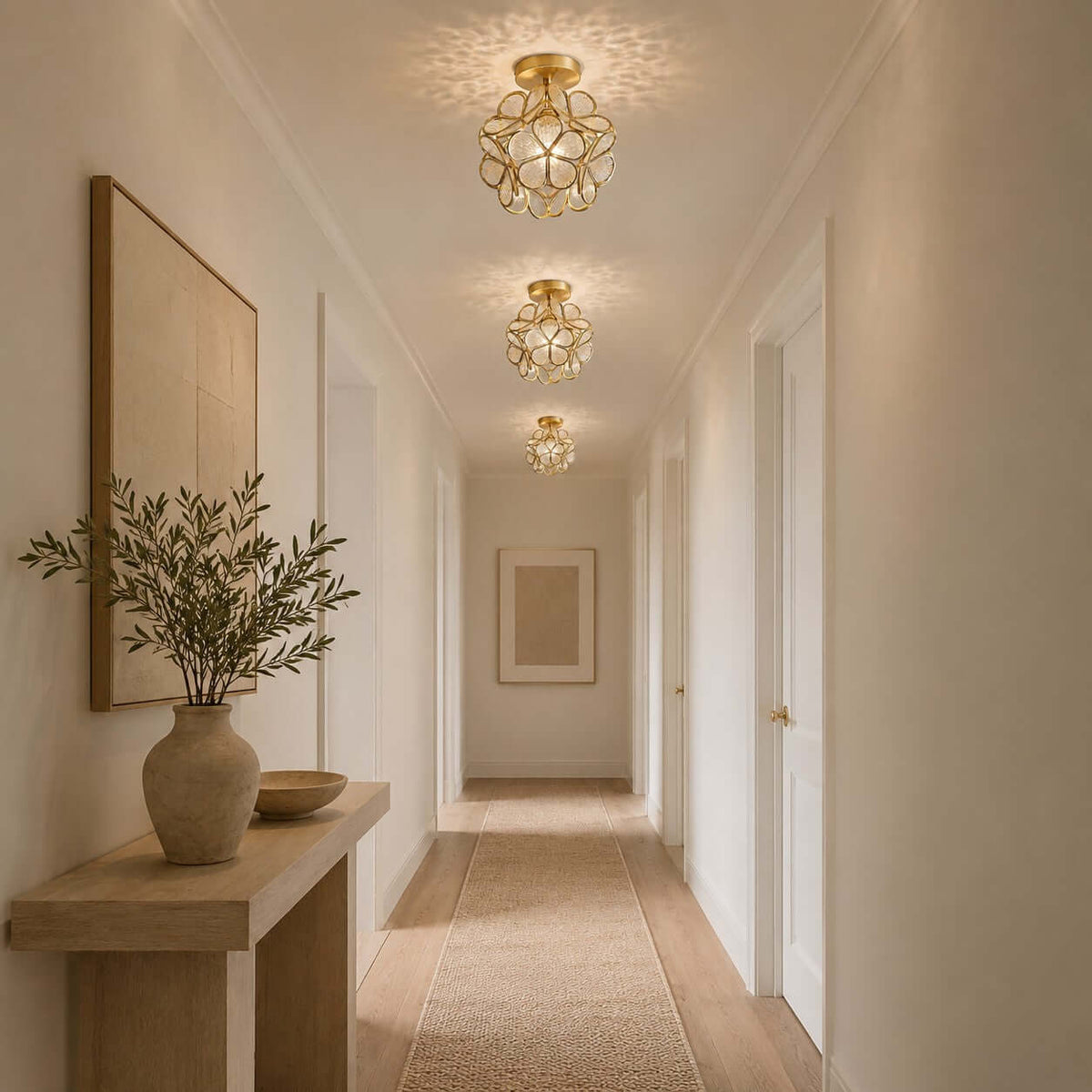 Three clear glass-petal Clérachic ceiling lights in a row along a long hallway, with a vase of olive branches on a console.