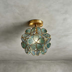 Blue-green glass-petal Clérachic ceiling light with a brass canopy, lit on a grey plaster ceiling.