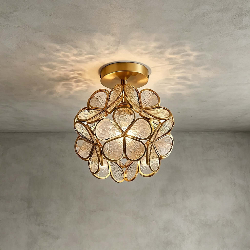 Clear textured glass-petal Clérachic ceiling light with a brass frame, throwing a dappled pattern on a grey plaster ceiling.