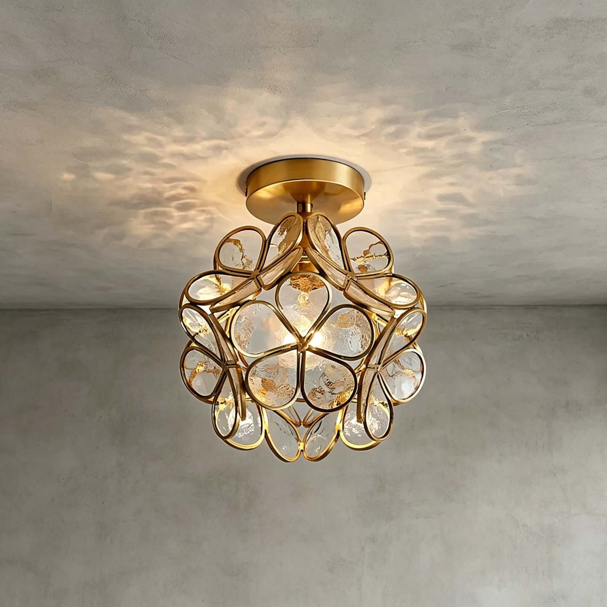Clear glass-petal Clérachic ceiling light with a few small crystal drops, casting a pattern on a grey plaster ceiling.