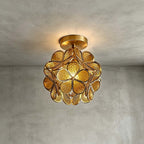 Honey-yellow glass-petal Clérachic ceiling light with textured petals and a brass frame, glowing on grey plaster.