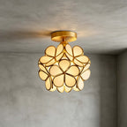 White glass-petal Clérachic ceiling light with a brass canopy, lit warm against a grey plaster wall and ceiling.