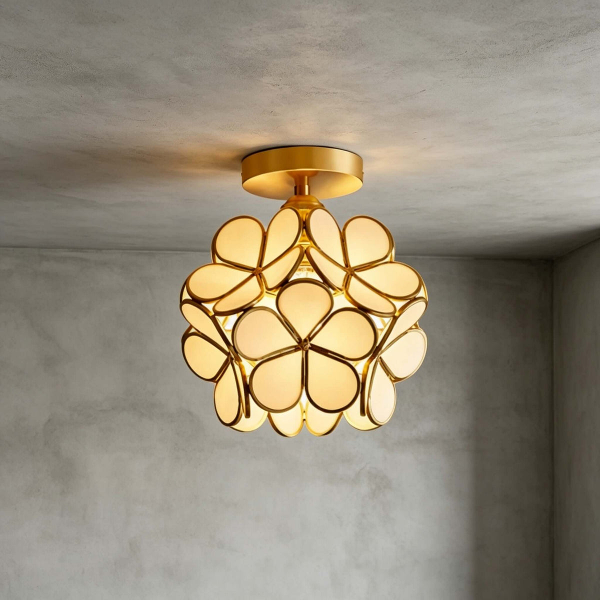 White glass-petal Clérachic ceiling light with a brass canopy, lit warm against a grey plaster wall and ceiling.