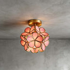 Pink glass-petal Clérachic ceiling light with a brass frame and canopy, lit against a grey plaster wall and ceiling.
