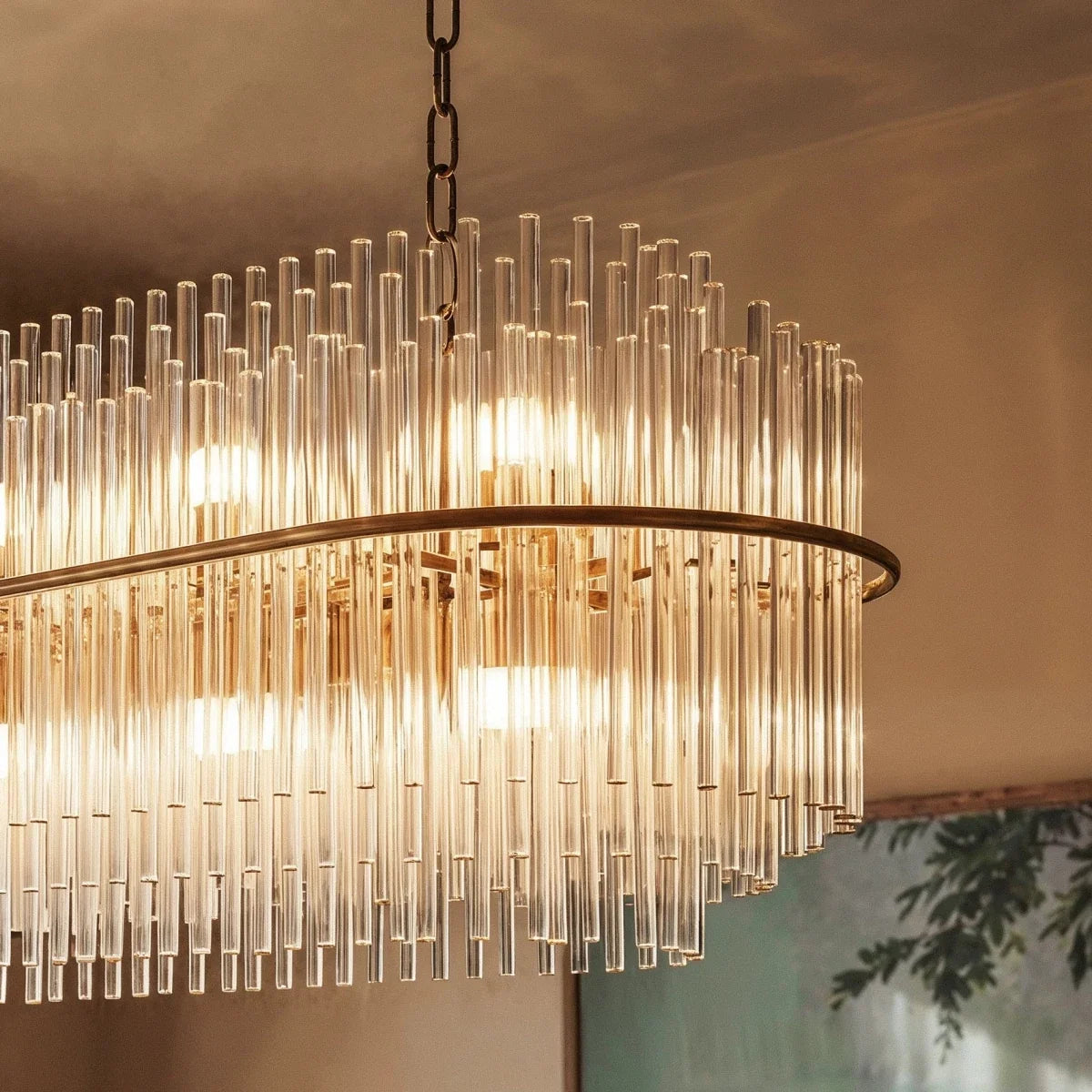 Close view of a Clérachic oval glass-rod chandelier: a gold band with clear rods above and below, lit from within.