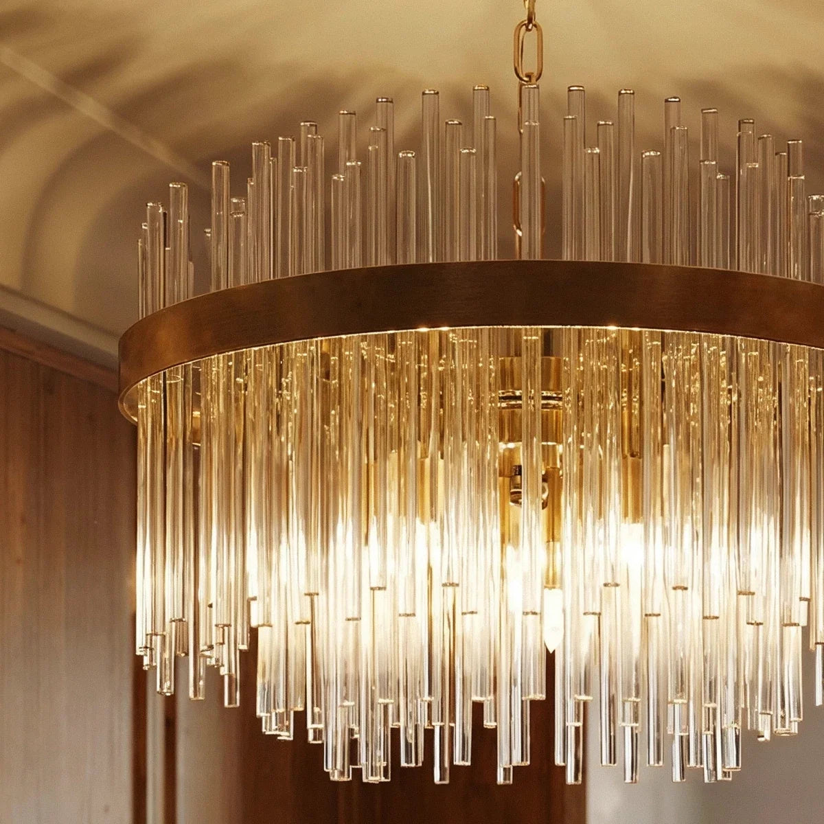 Close-up of the Clérachic round chandelier: a gold ring, clear glass rods in tiers and warm light glowing through them.