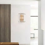 A Clérachic glass-rod wall light on a white wall beside a dark wood panel, with a bright doorway and a pale bench in the room beyond.