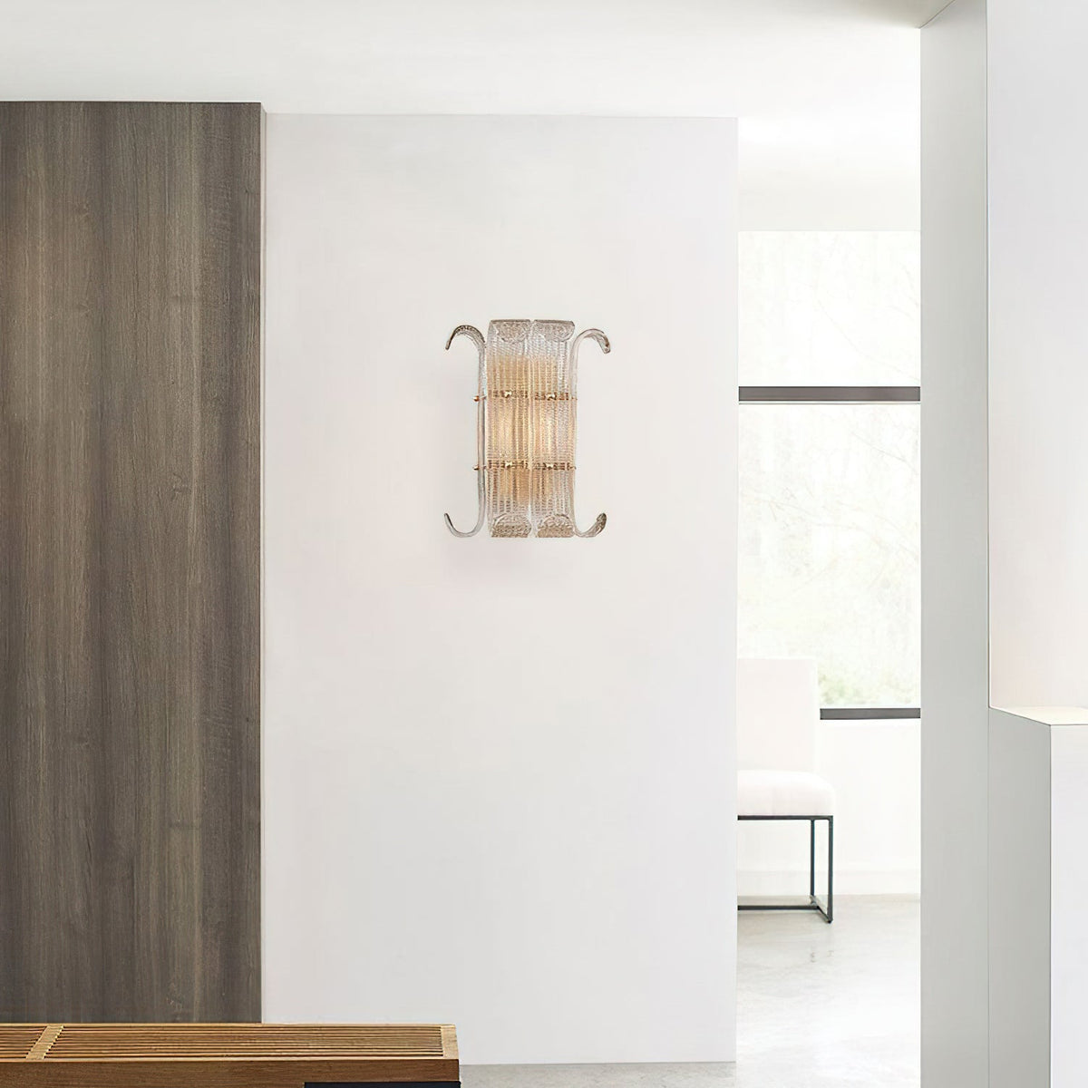 A Clérachic glass-rod wall light on a white wall beside a dark wood panel, with a bright doorway and a pale bench in the room beyond.
