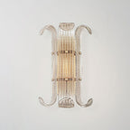 Straight-on view of this Clérachic wall light, a narrow ribbed glass shade with curled arms, lit warm against a soft grey wall.