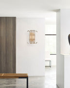 A small Clérachic glass-rod wall light on a white wall in a bright hallway, with a wooden bench and a grey stone floor in the foreground.