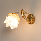 Clérachic glass rose wall sconce lit on a warm plaster wall, the cast brass cherub reaching up to hold the glowing opal flower.