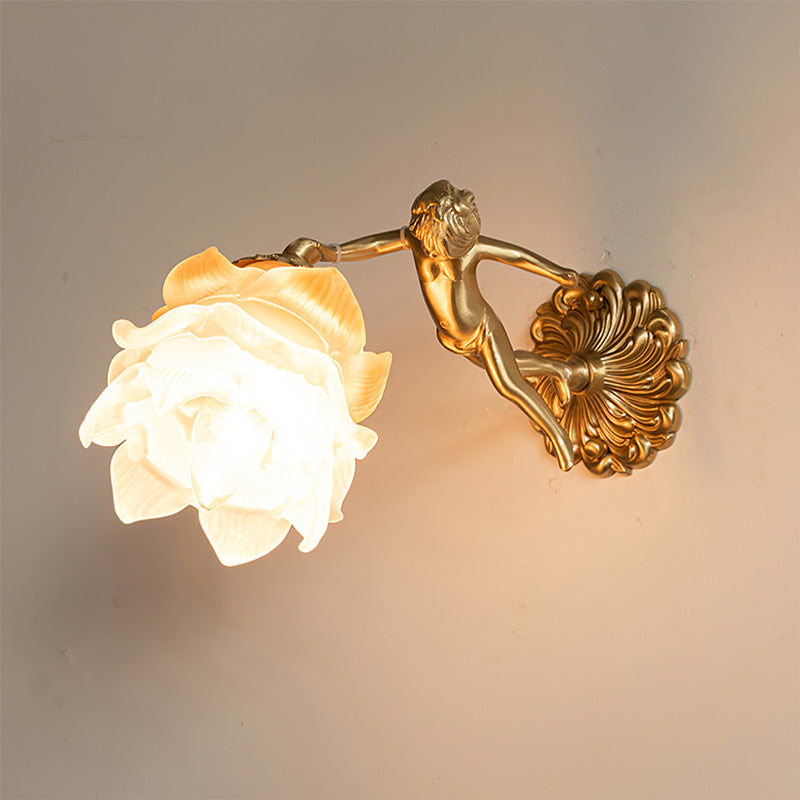 Clérachic glass rose wall sconce lit on a warm plaster wall, the cast brass cherub reaching up to hold the glowing opal flower.