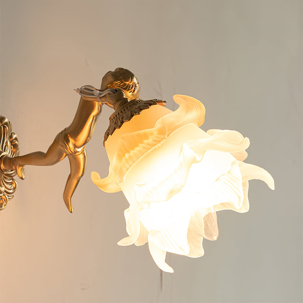 Close-up of the lit Clérachic glass rose wall sconce, where the brass gallery collar grips the layered glass petals above the cherub.