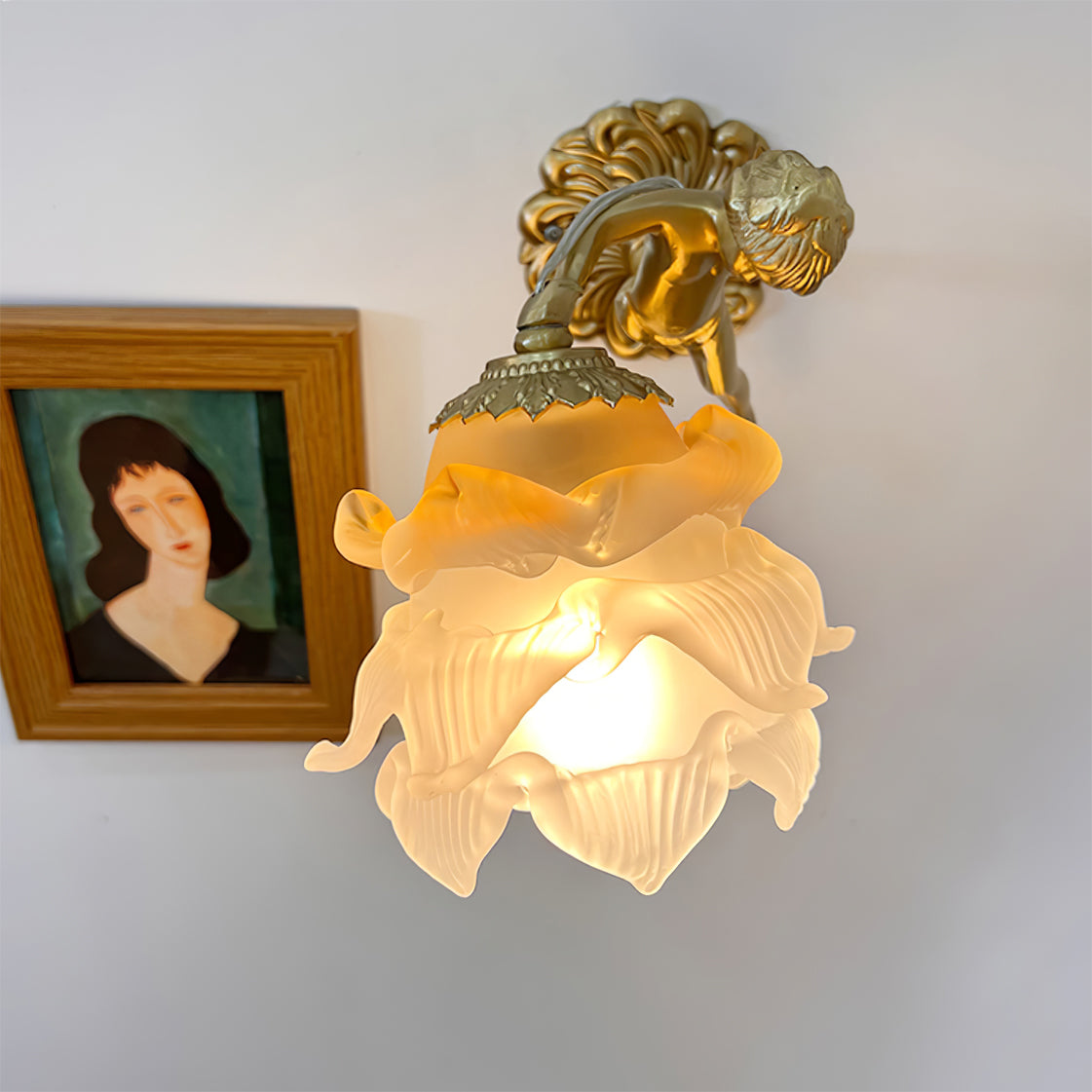 The Clérachic glass rose wall sconce lit beside a framed portrait, its ruffled petals fanning out below the scalloped brass collar.