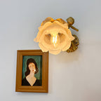 Head-on view of the Clérachic glass rose wall sconce with the candle bulb visible inside the open flower above a framed portrait.