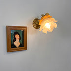 Clérachic glass rose wall sconce lit on a grey bedroom wall next to a framed portrait, reading as a soft accent rather than a room light.