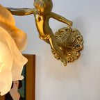 Detail of the Clérachic glass rose wall sconce from below, showing the cast brass cherub stretched between the shade and round backplate.