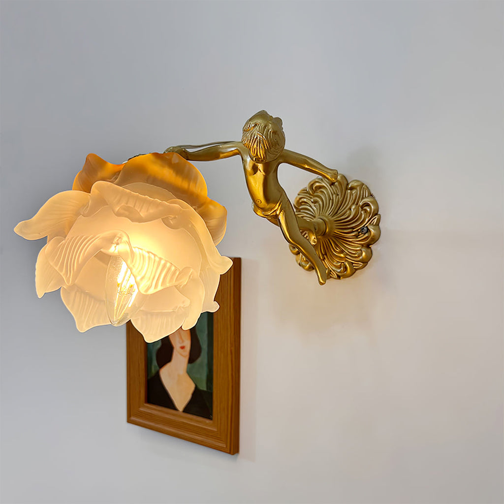 Three-quarter view of the Clérachic glass rose wall sconce lit above a framed portrait, candle bulb glowing through the layered petals.