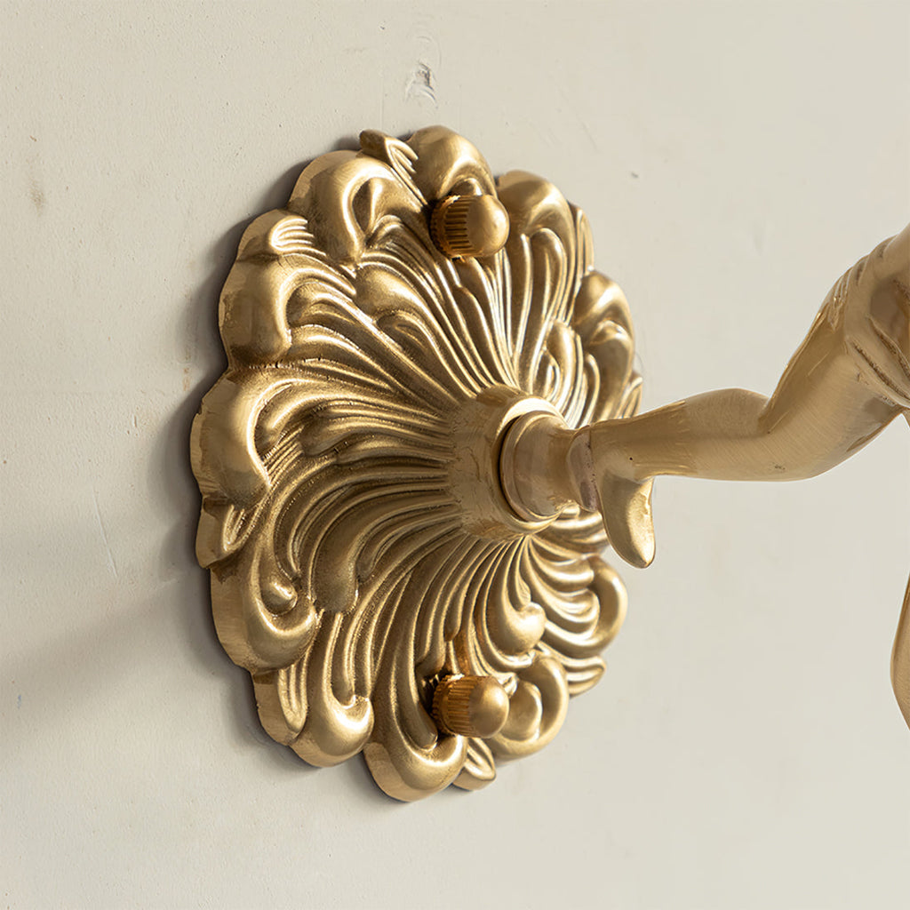 Detail of the Clérachic glass rose wall sconce backplate — a scalloped brass acanthus disc fixed by two knurled thumb screws.