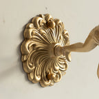 Detail of the Clérachic glass rose wall sconce backplate — a scalloped brass acanthus disc fixed by two knurled thumb screws.