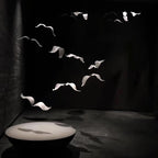 This Clérachic seagull chandelier scatters pale glass birds across a black room, their shadows falling on a low round table.